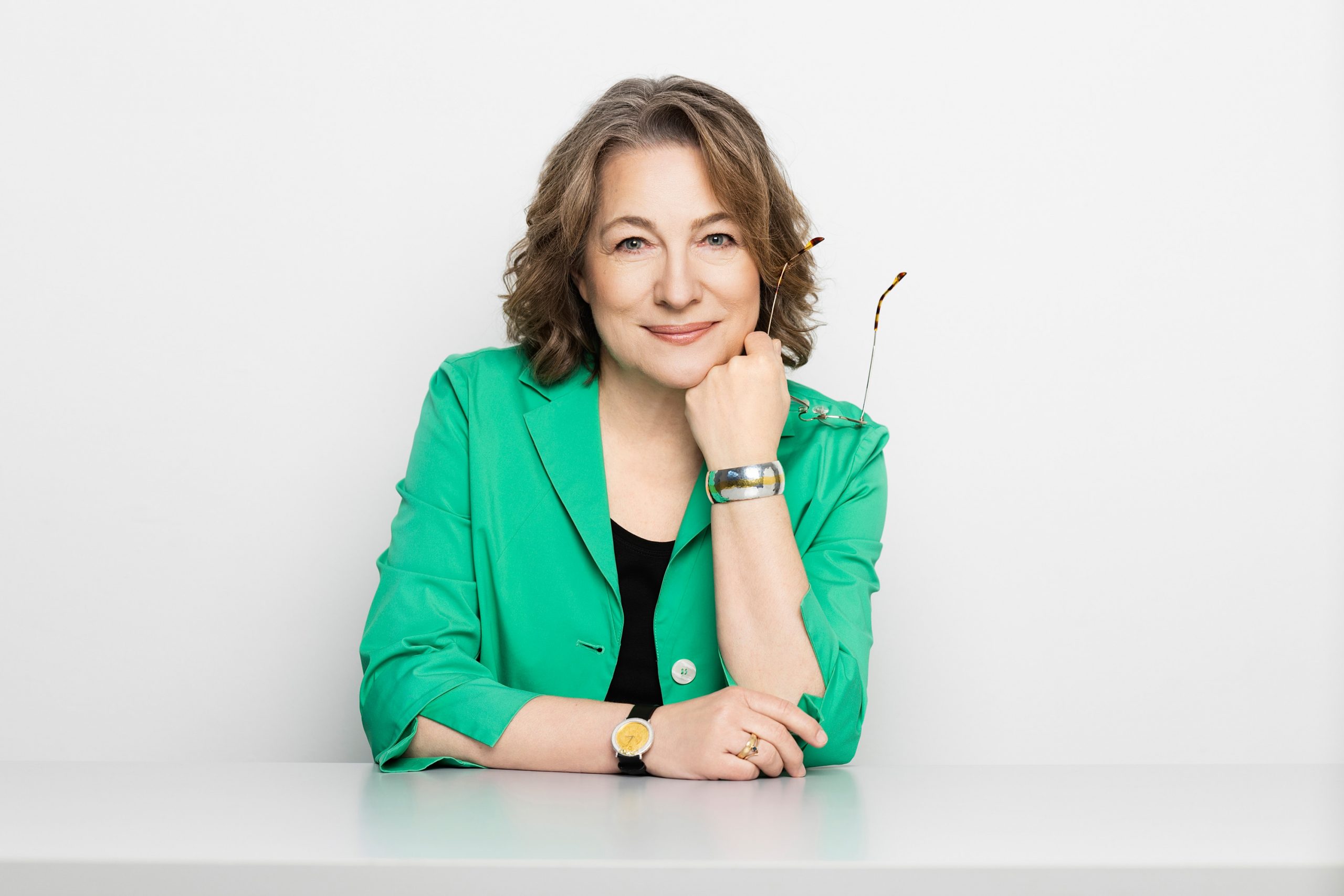 Businessfrau am Tisch sitzend Arm aufgelehnt Arm abgestützt mit Brille in der Hand